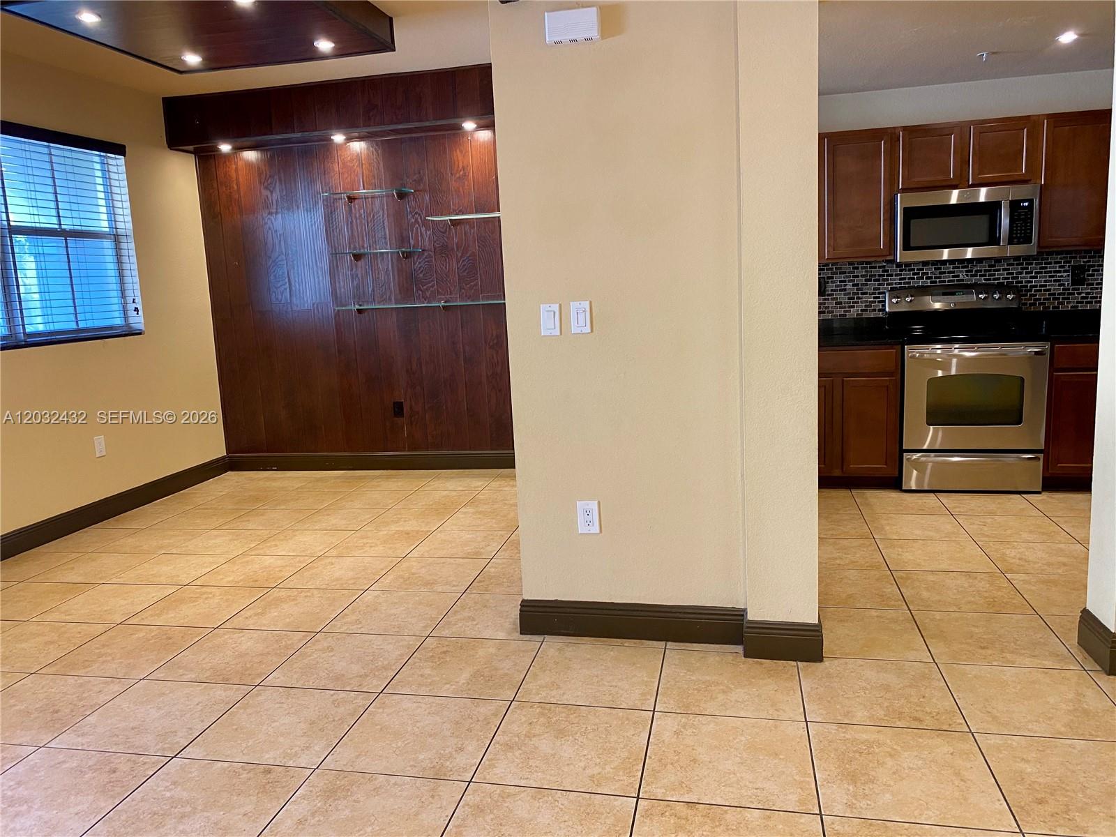 A room with tile floors features a wood-paneled accent wall and an adjacent kitchen — 8800 NW 107th CT # 110, Doral FL 33178, DORAL, FL