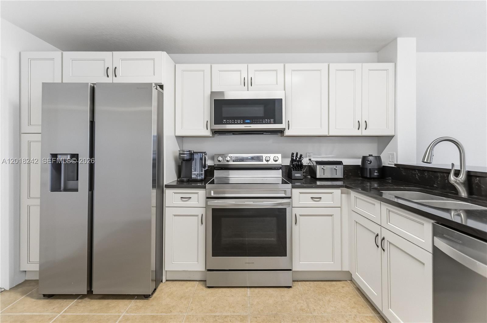 A kitchen features white cabinetry, stainless steel appliances, and dark countertops over tile flooring — 4065 Crystal Lake Dr, Deerfield Beach FL 33064, DEERFIELD BEACH, FL