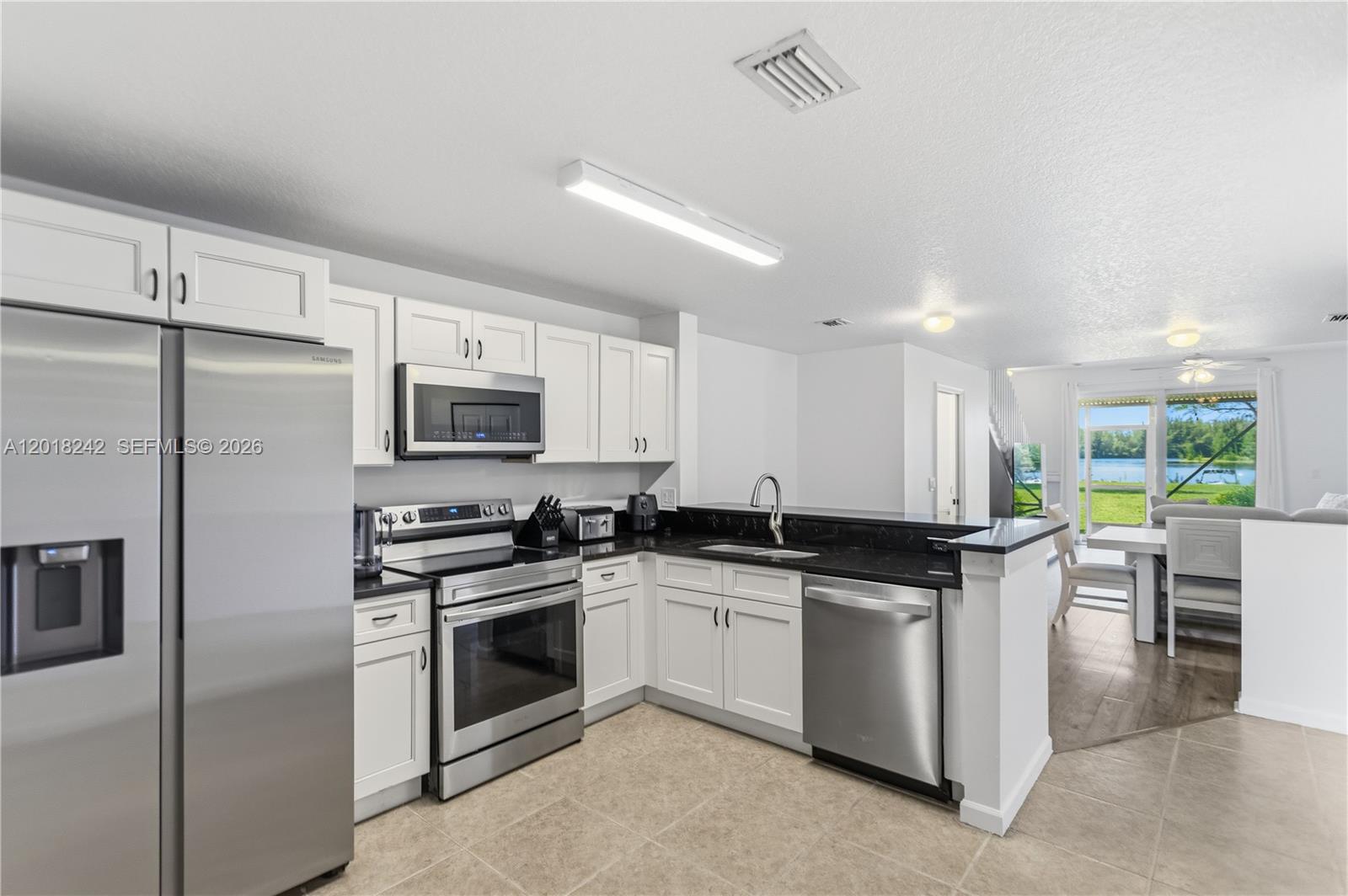 A kitchen with white cabinets, stainless steel appliances, and black countertops overlooks a dining area — 4065 Crystal Lake Dr, Deerfield Beach FL 33064, DEERFIELD BEACH, FL