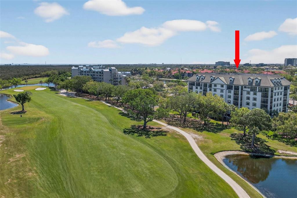 An aerial view shows a multi-story apartment building situated next to a golf course — 14820 RUE DE BAYONNE UNIT 302, CLEARWATER, FL