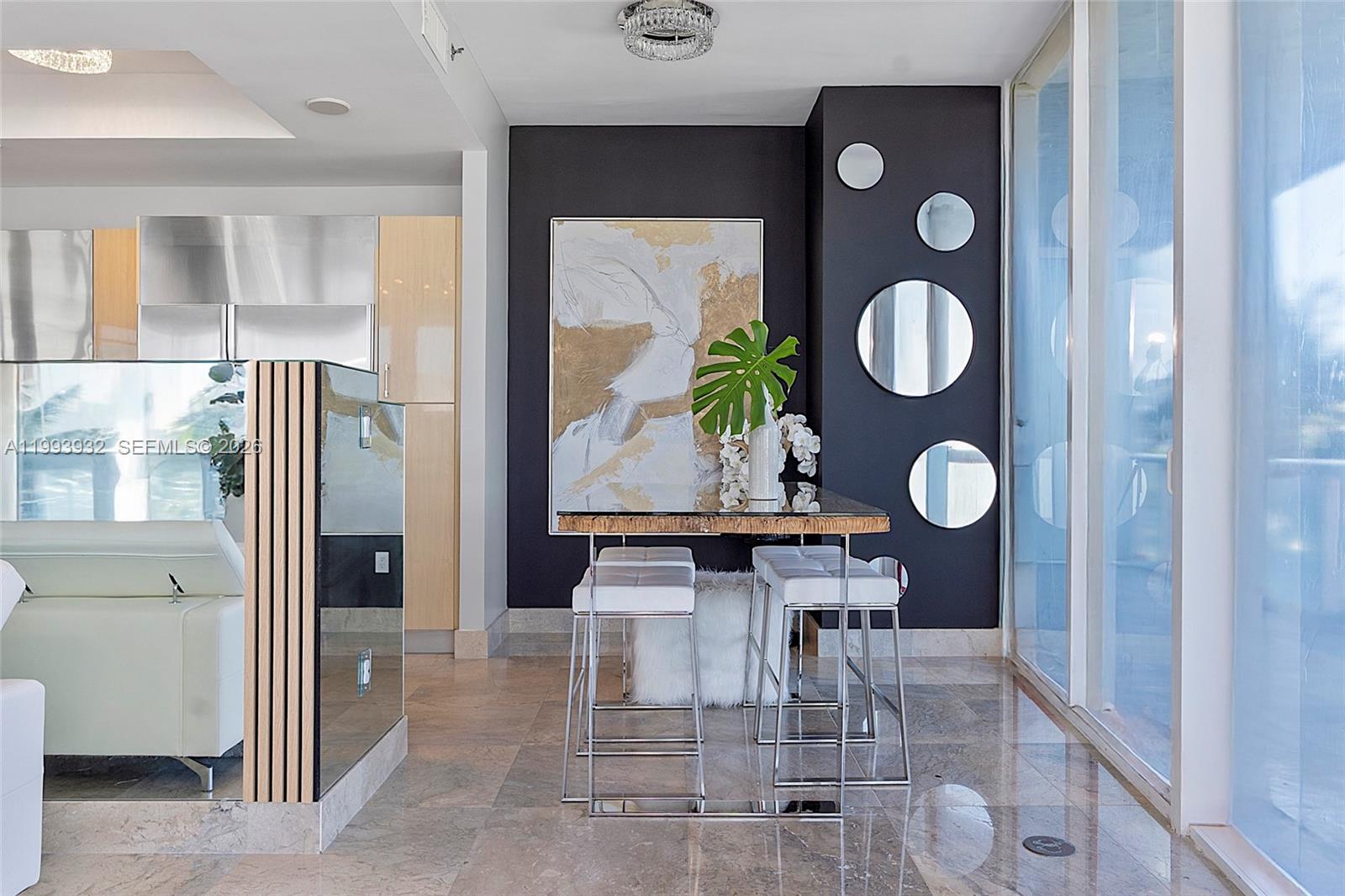 A dining area features a glass-topped table, white stools, and circular mirrors on a dark wall — 100 S Pointe Dr # 506, Miami Beach FL 33139, MIAMI BEACH, FL