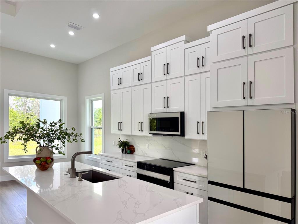 A modern kitchen features white cabinetry, a quartz island with a sink, and stainless appliances — 30 WOOD CEDAR DR, PALM COAST, FL