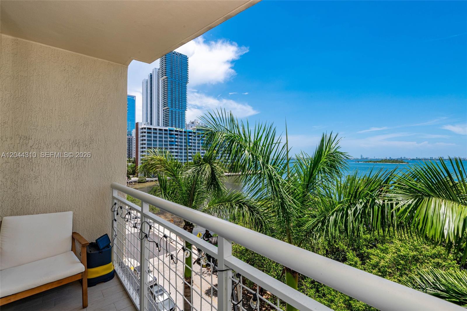 A balcony with a white chair overlooks palm trees, a waterway, and city skyscrapers — 2000 N Bayshore Dr # 516, Miami FL 33137, MIAMI, FL