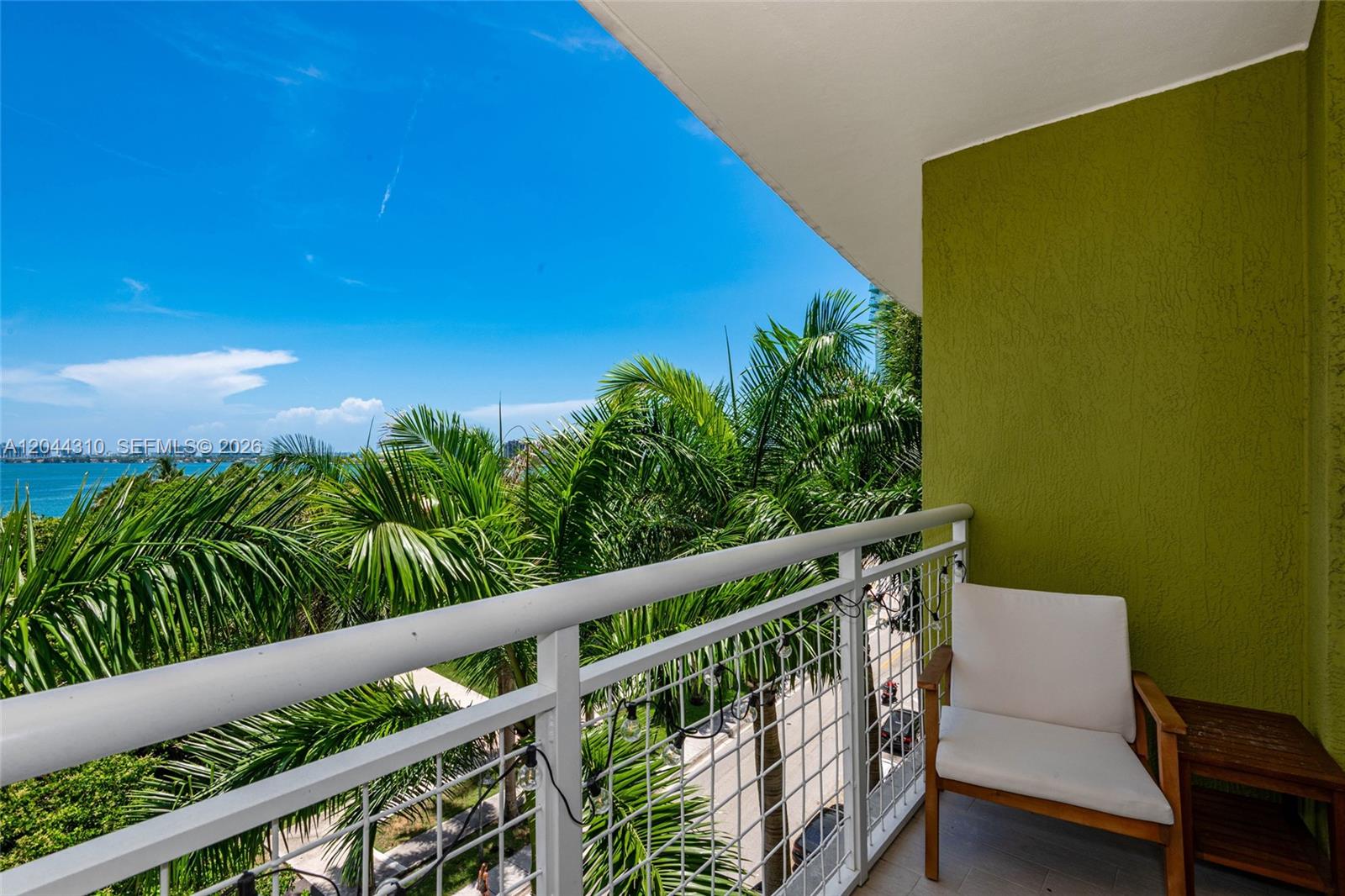 A balcony with a white chair, string lights, and a view of palm trees and water — 2000 N Bayshore Dr # 516, Miami FL 33137, MIAMI, FL
