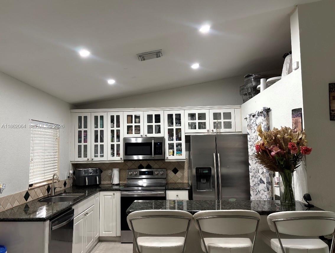 A kitchen features white cabinets, stainless steel appliances, dark granite countertops, and a breakfast bar — 20990 SW 119th Ct, Miami FL 33177, MIAMI, FL