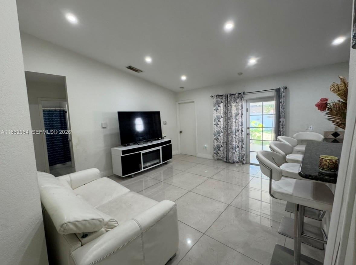 A living room features white tile floors, a white sofa, a television console, and bar seating — 20990 SW 119th Ct, Miami FL 33177, MIAMI, FL