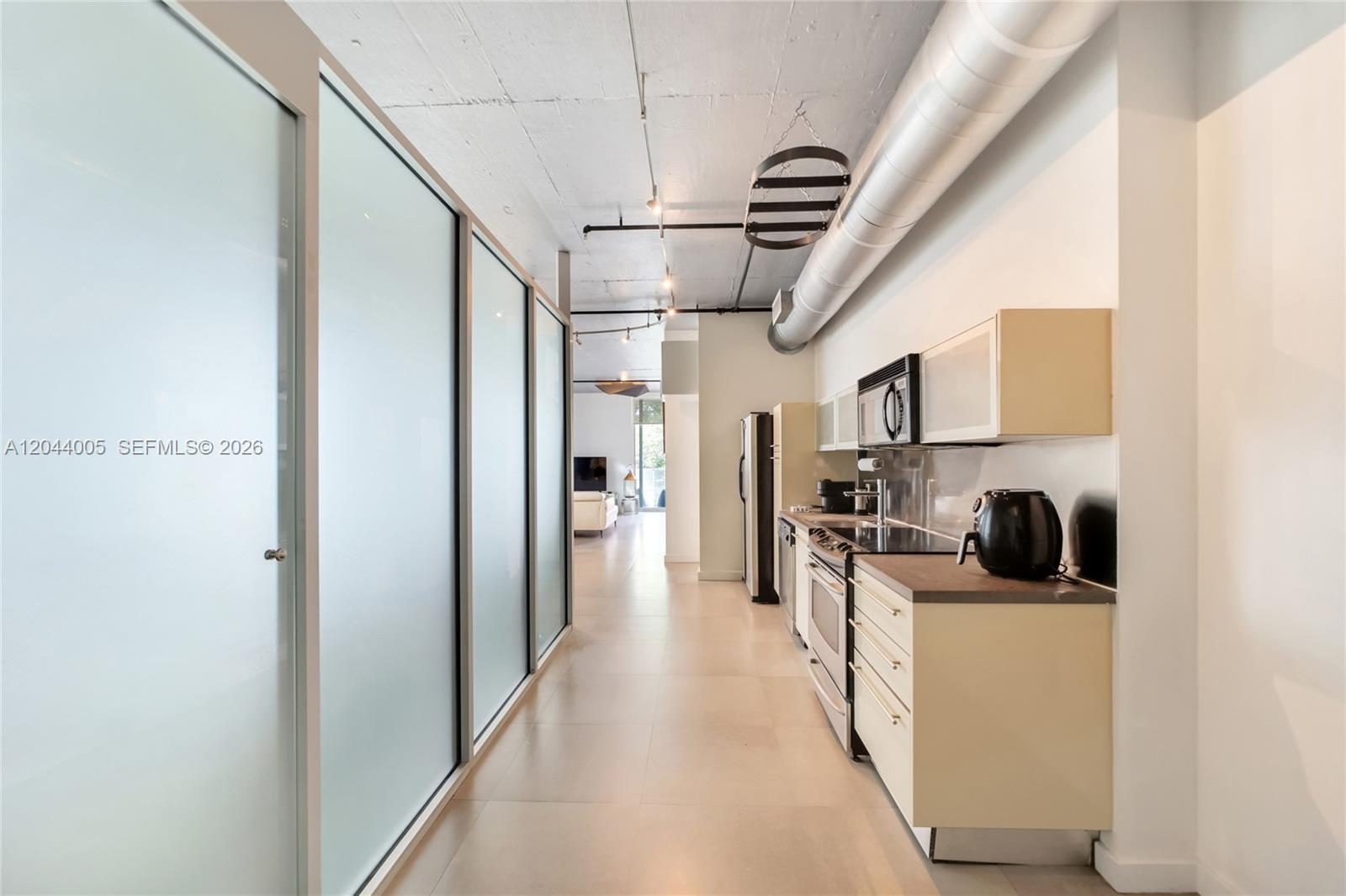 A galley kitchen features light-colored cabinets, stainless steel appliances, and an exposed concrete ceiling — 1700 Meridian Ave # 310, Miami Beach FL 33139, MIAMI BEACH, FL