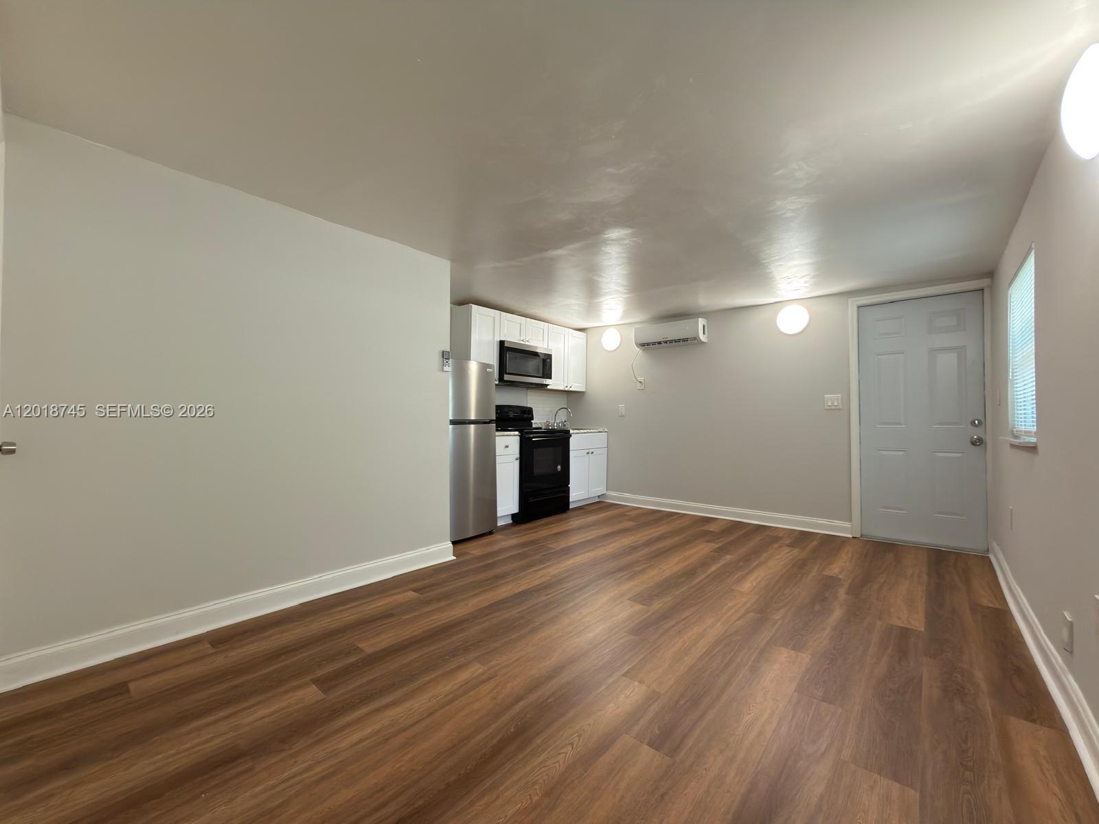 This studio apartment features wood-look flooring, white kitchen cabinetry, and a wall-mounted air conditioner — 10335 NW 2nd Ct # 3, Miami FL 33150, MIAMI, FL