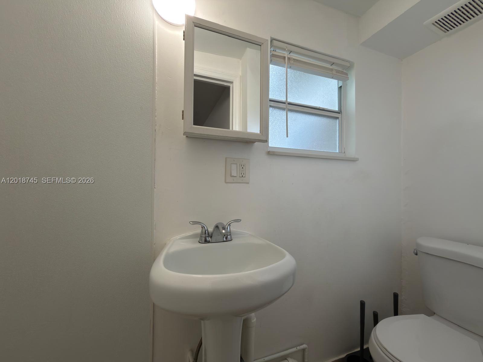 A small bathroom features a pedestal sink, a medicine cabinet, a window, and a toilet — 10335 NW 2nd Ct # 3, Miami FL 33150, MIAMI, FL