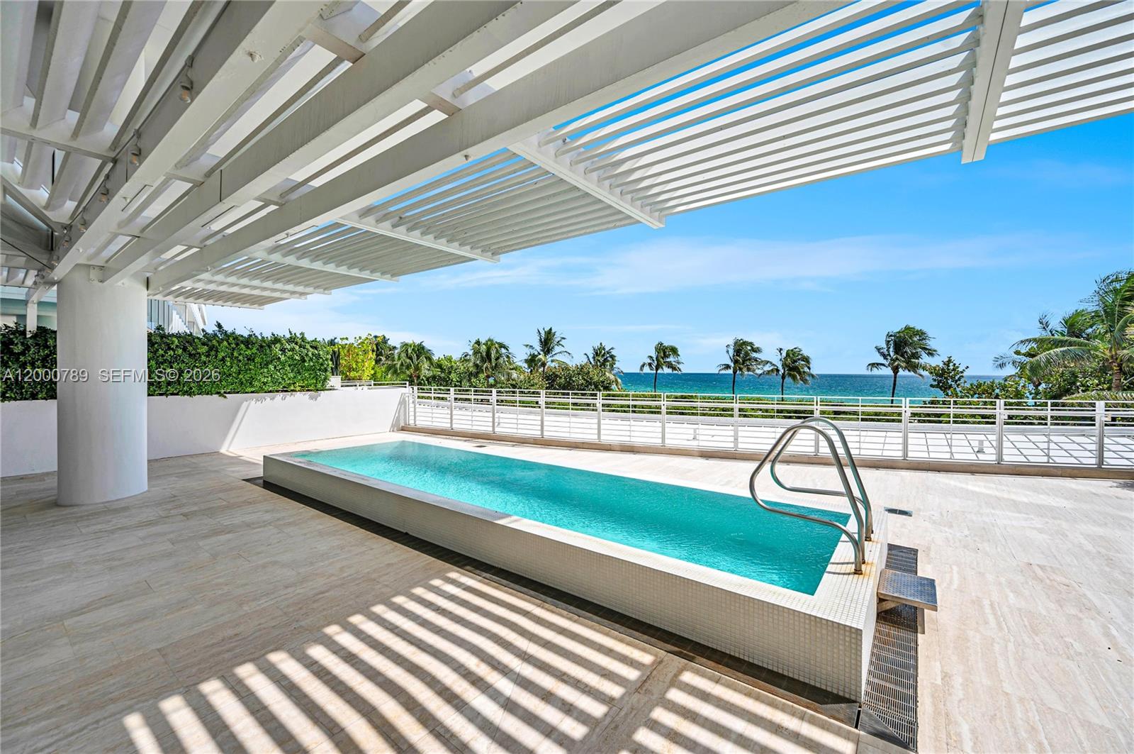 A rectangular swimming pool sits on a tiled terrace beneath a white slatted pergola — 9001 Collins Ave # 201, Surfside FL 33154, SURFSIDE, FL