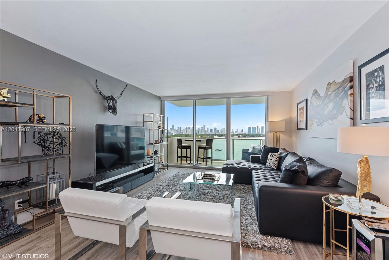 A modern living room features a black sectional sofa, white armchairs, and a balcony view — 1200 West Ave # 1005, Miami Beach FL 33139, MIAMI BEACH, FL