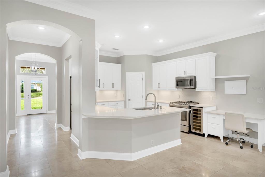 A bright kitchen features white cabinets, quartz countertops, a center island, and an attached desk area — 8507 BOWDEN WAY, WINDERMERE, FL