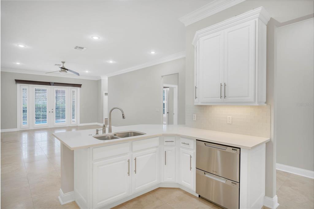 A kitchen island with a double sink and stainless steel dishwasher in a white kitchen — 8507 BOWDEN WAY, WINDERMERE, FL