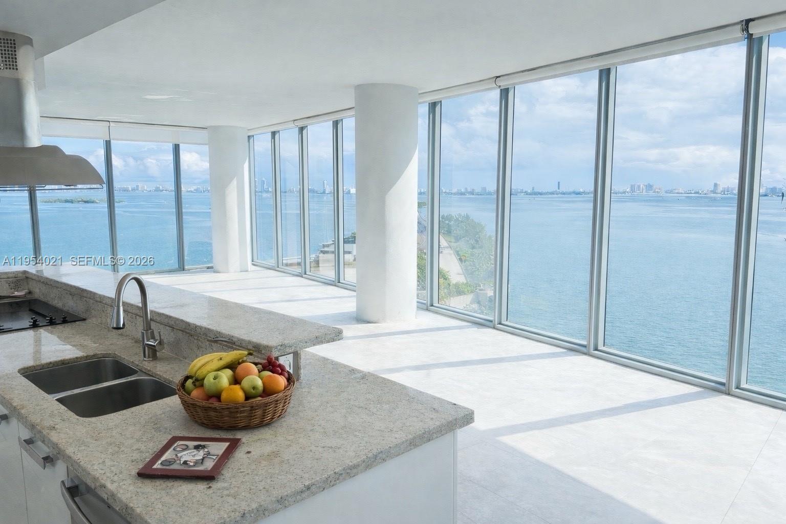 A kitchen with granite countertops overlooks a large body of water through floor-to-ceiling windows — 601 NE 36th St # 1112, Miami FL 33137, MIAMI, FL