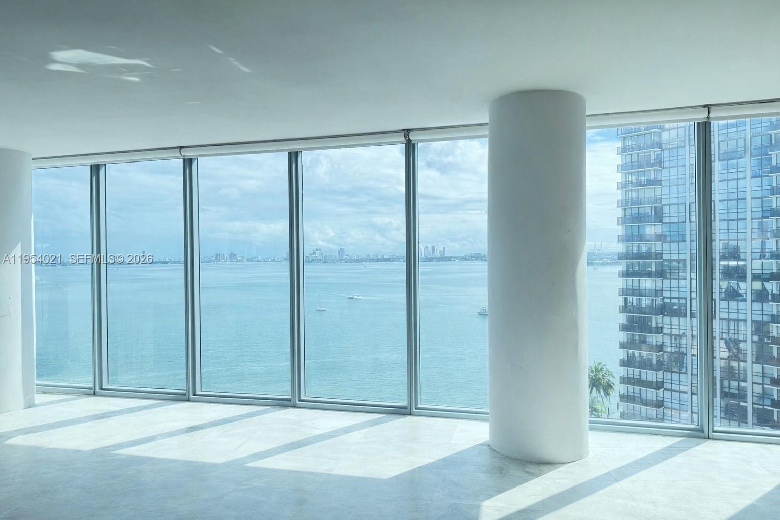 A bright, empty room features floor-to-ceiling windows with expansive ocean and city skyline views — 601 NE 36th St # 1112, Miami FL 33137, MIAMI, FL