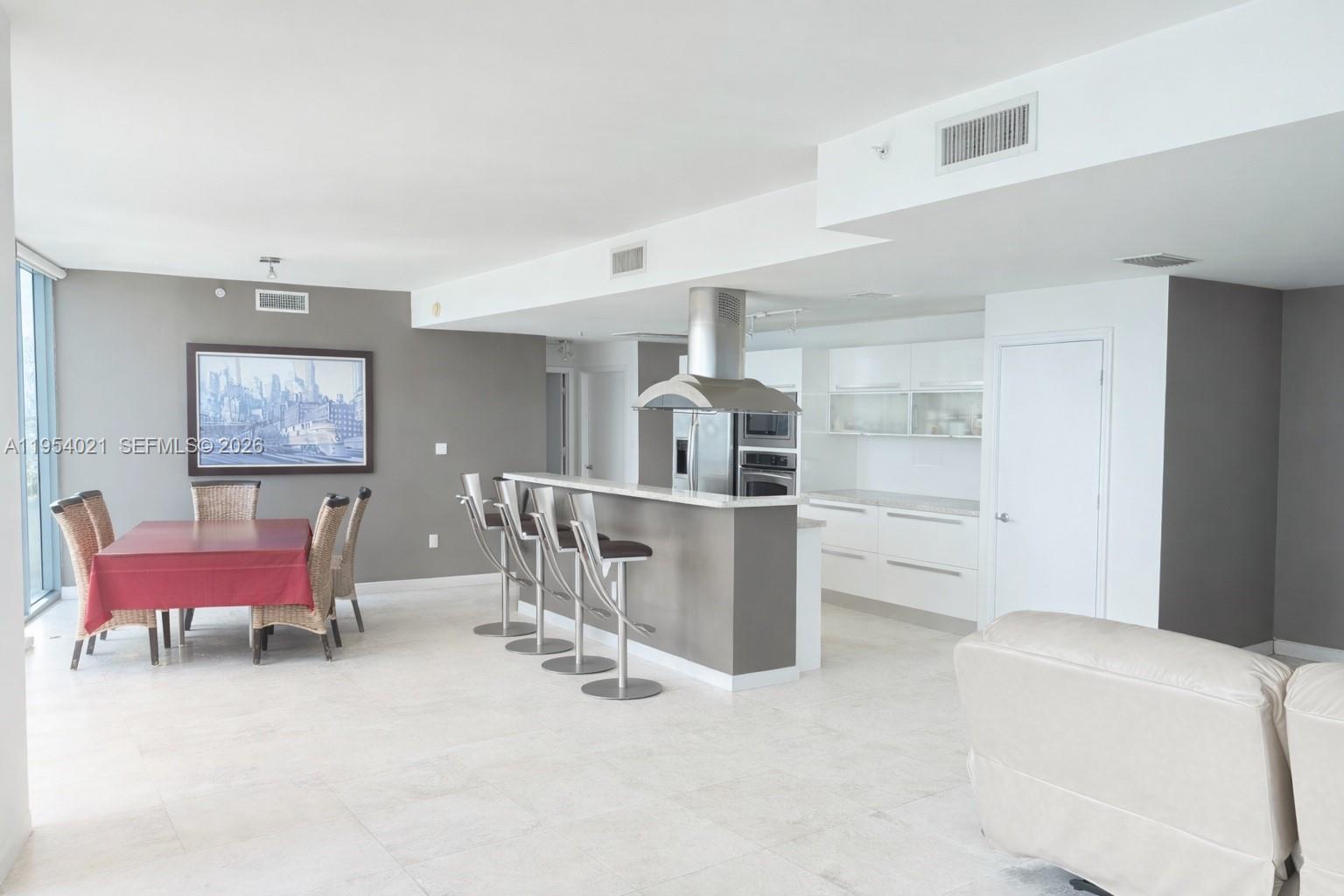 An open-concept kitchen with a breakfast bar and dining area features white cabinets and tile — 601 NE 36th St # 1112, Miami FL 33137, MIAMI, FL