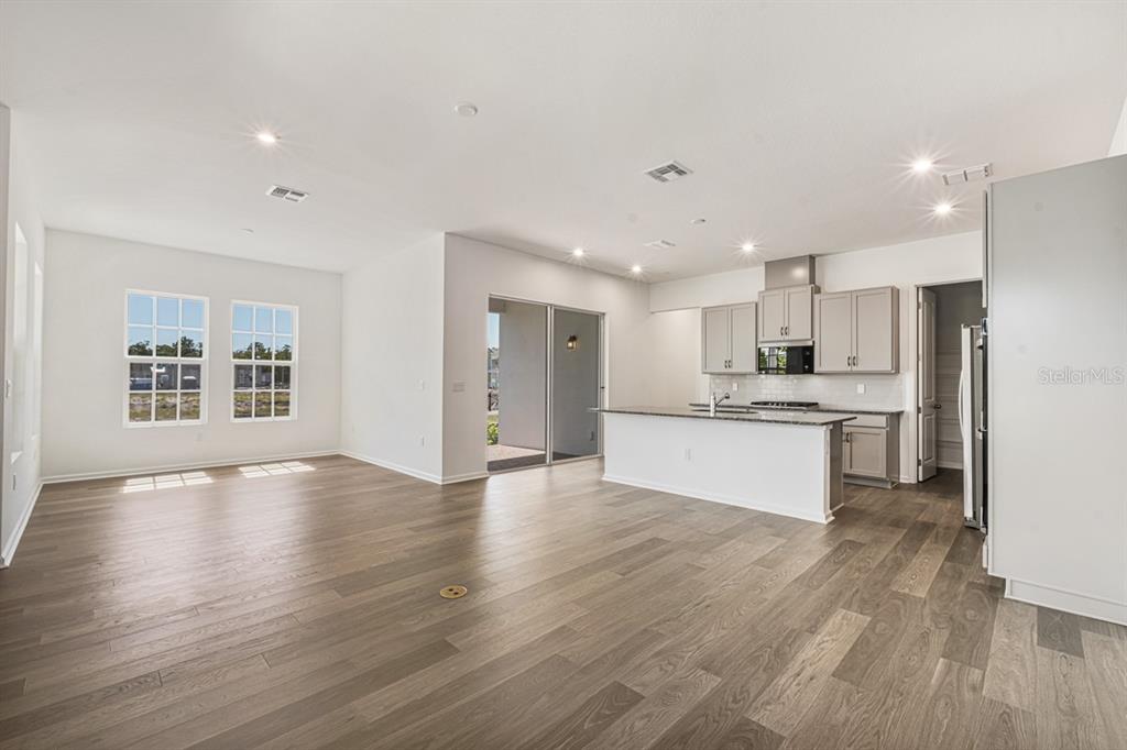 An open-concept kitchen and living area features light gray cabinetry, granite countertops, and wood flooring — 1833 HEADLAND LOOP, KISSIMMEE, FL