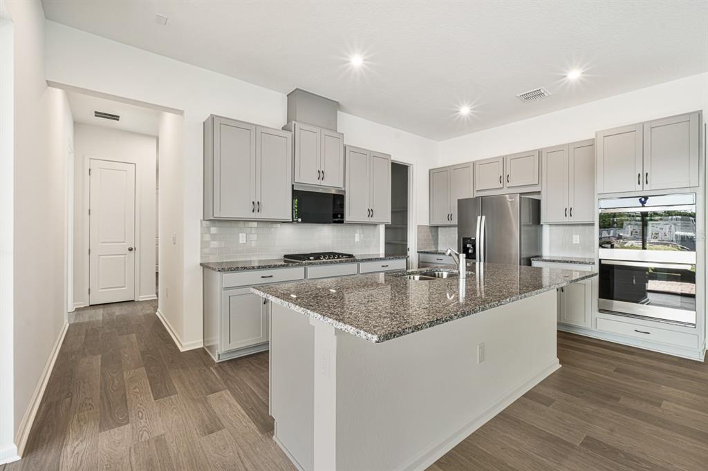 A modern kitchen features gray cabinets, granite countertops, a central island, and stainless steel appliances — 1833 HEADLAND LOOP, KISSIMMEE, FL