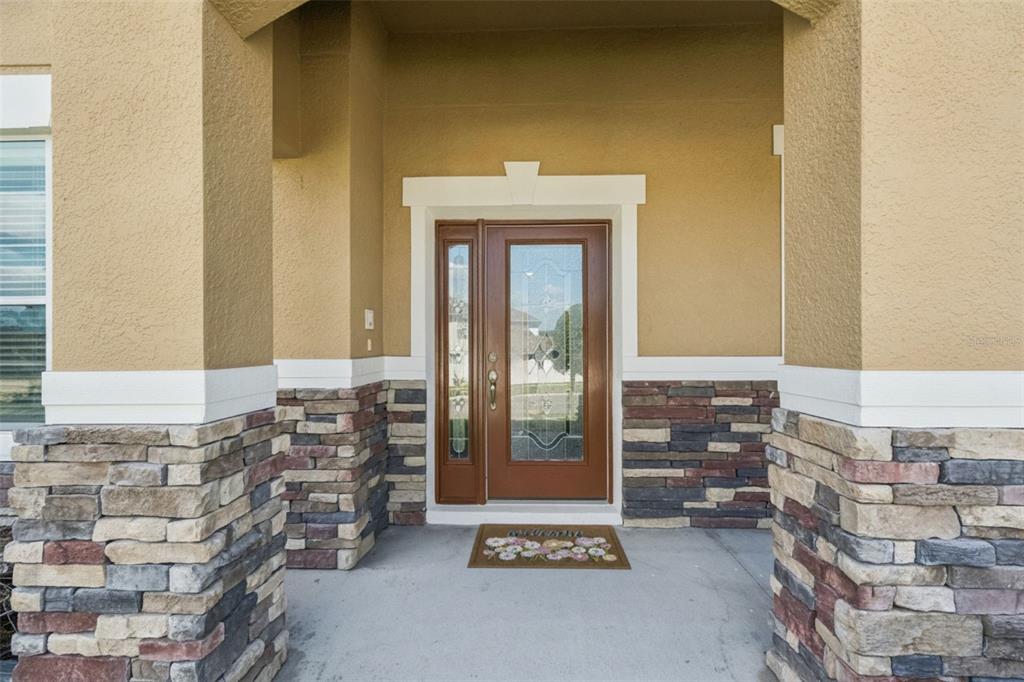 A front entryway features a brown glass-paneled door flanked by stone-clad pillars and stucco walls — 11121 LEMAY DRIVE, CLERMONT, FL