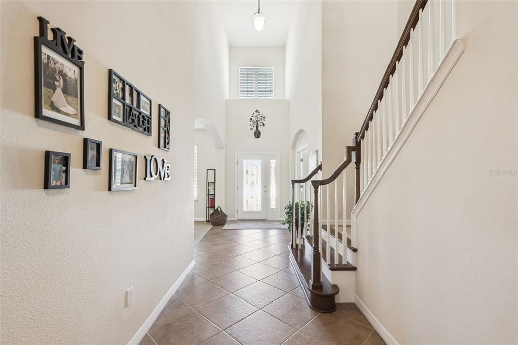 A tiled entryway features a high ceiling, a staircase with a wooden railing, and wall decor — 11121 LEMAY DRIVE, CLERMONT, FL