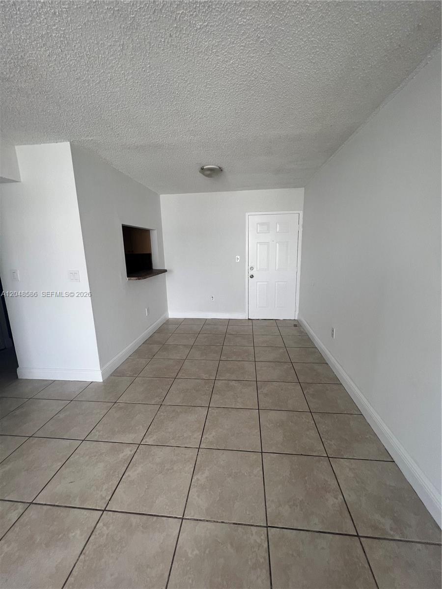 An empty room features white walls, a tiled floor, and a small kitchen pass-through window — 8145 NW 7th St # 405, Miami FL 33126, MIAMI, FL