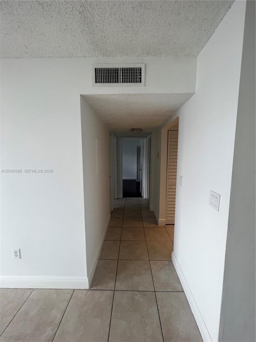 A hallway with white walls and light-colored tile flooring leads toward a dark-floored room — 8145 NW 7th St # 405, Miami FL 33126, MIAMI, FL
