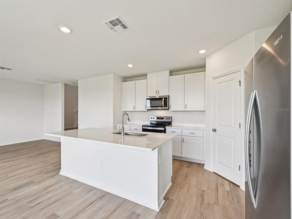A modern kitchen features white cabinets, a quartz island with a sink, and stainless appliances — 11259 BELLEWOOD TERRACE, PARRISH, FL