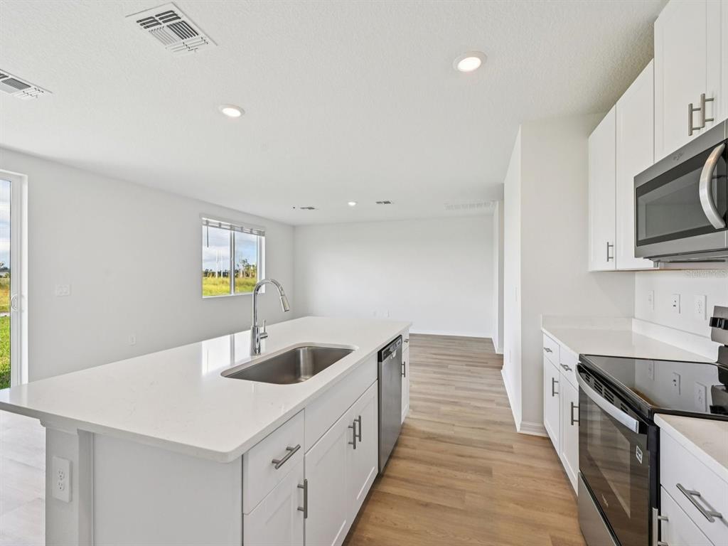 A modern kitchen features white cabinets, quartz countertops, a center island, and wood-look flooring — 11259 BELLEWOOD TERRACE, PARRISH, FL