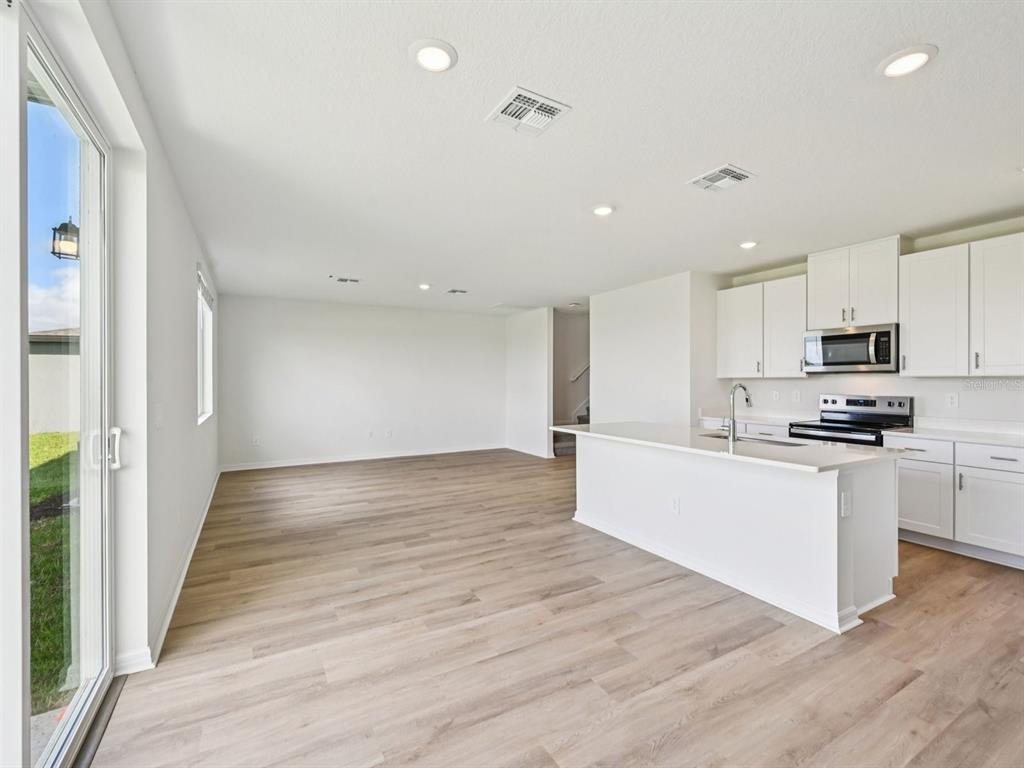 A bright, open-concept kitchen and living area featuring white cabinetry, an island, and wood-look flooring — 11259 BELLEWOOD TERRACE, PARRISH, FL