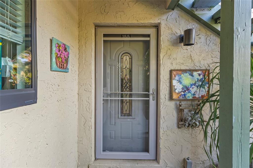 A beige stucco exterior wall features a front door with a decorative glass storm door — 1520 PELICAN POINT DRIVE UNIT 155, SARASOTA, FL