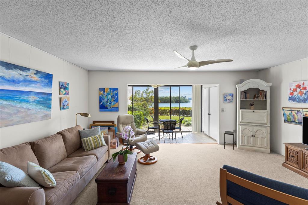 A living room with a brown sofa, beige carpet, and sliding doors leading to a patio — 1520 PELICAN POINT DRIVE UNIT 155, SARASOTA, FL