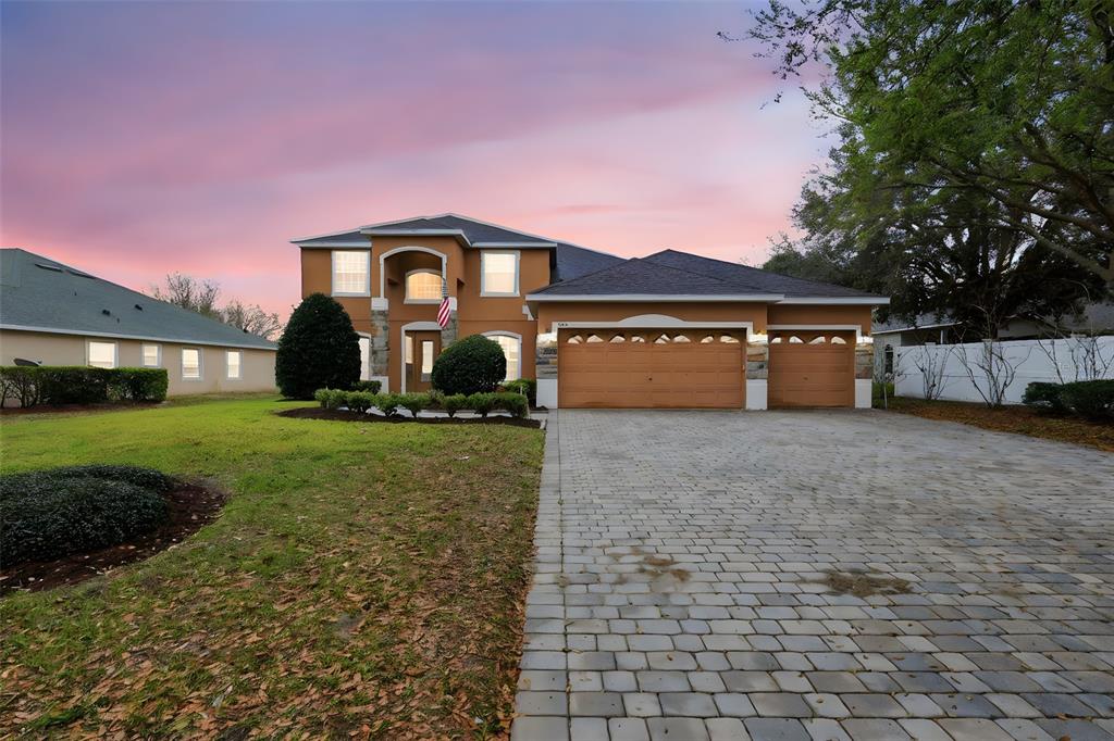 A two-story house with a paved driveway, three-car garage, and stone accents at sunset — 1042 SPINNING WHEEL DRIVE, APOPKA, FL