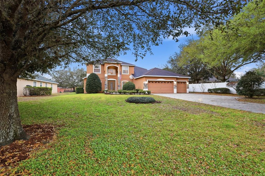 A two-story house with a tan stucco exterior, a three-car garage, and a large lawn — 1042 SPINNING WHEEL DRIVE, APOPKA, FL