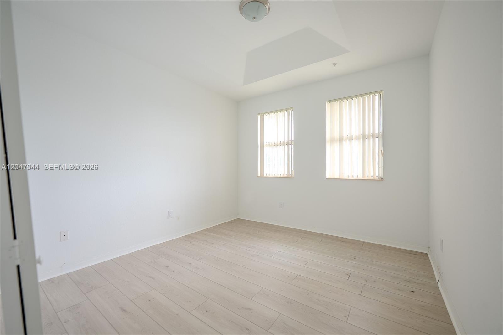 An empty room features white walls, light wood-look flooring, and two windows with vertical blinds — 10855 NW 88th Ter # 212, Doral FL 33178, DORAL, FL