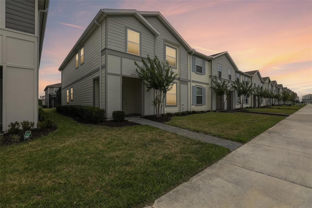 A row of two-story townhouses with light-colored siding and small front lawns at sunset — 4290 LANA AVENUE, DAVENPORT, FL