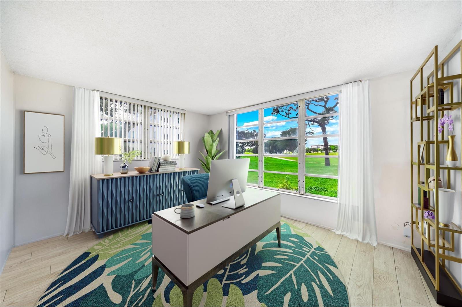 A home office features a desk, a blue sideboard, and a large window overlooking greenery — 2601 S Course Drive # 111, Pompano Beach FL 33069, POMPANO BEACH, FL