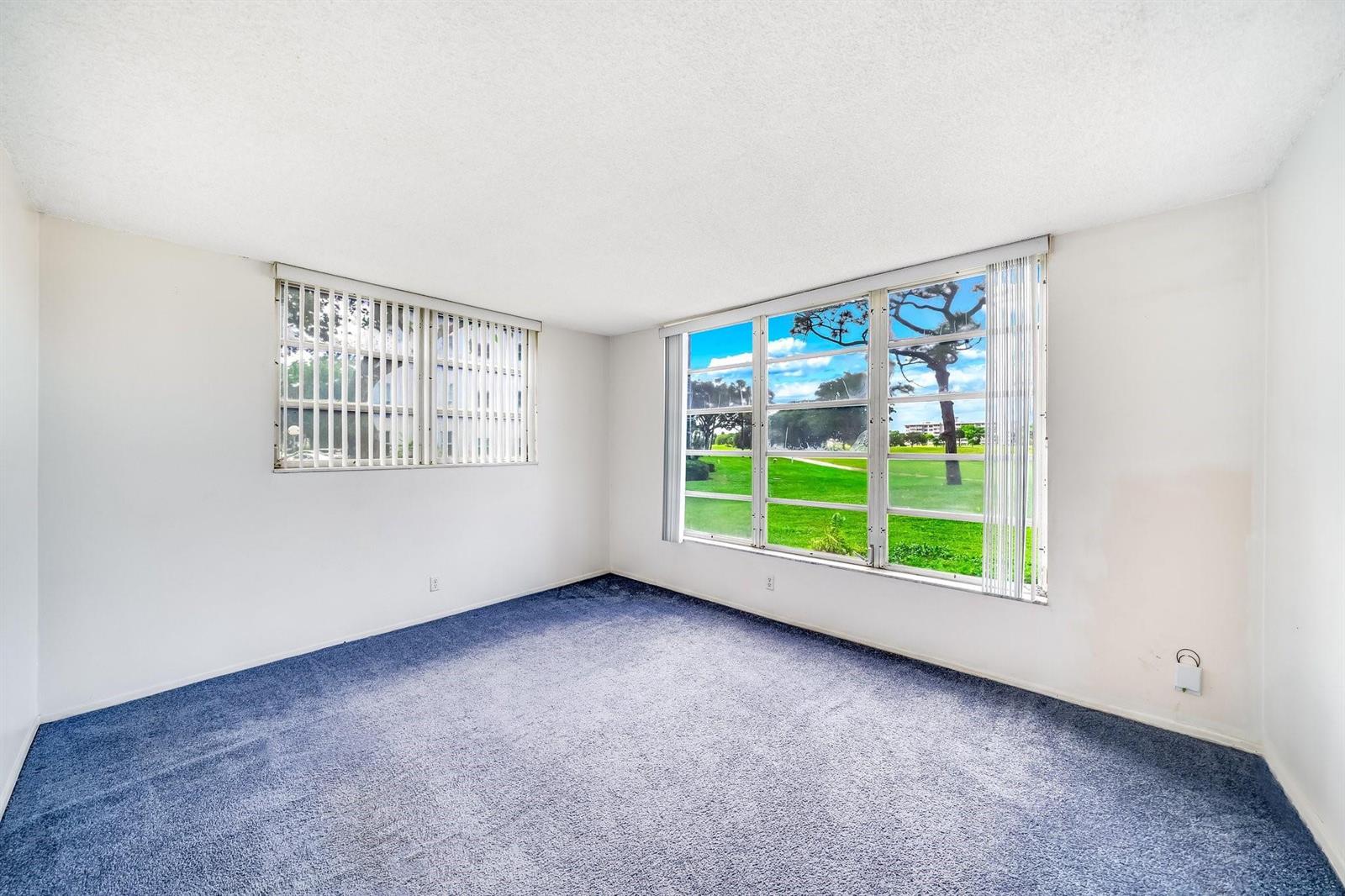 An empty room with blue carpeting, white walls, and two windows overlooking a golf course — 2601 S Course Drive # 111, Pompano Beach FL 33069, POMPANO BEACH, FL