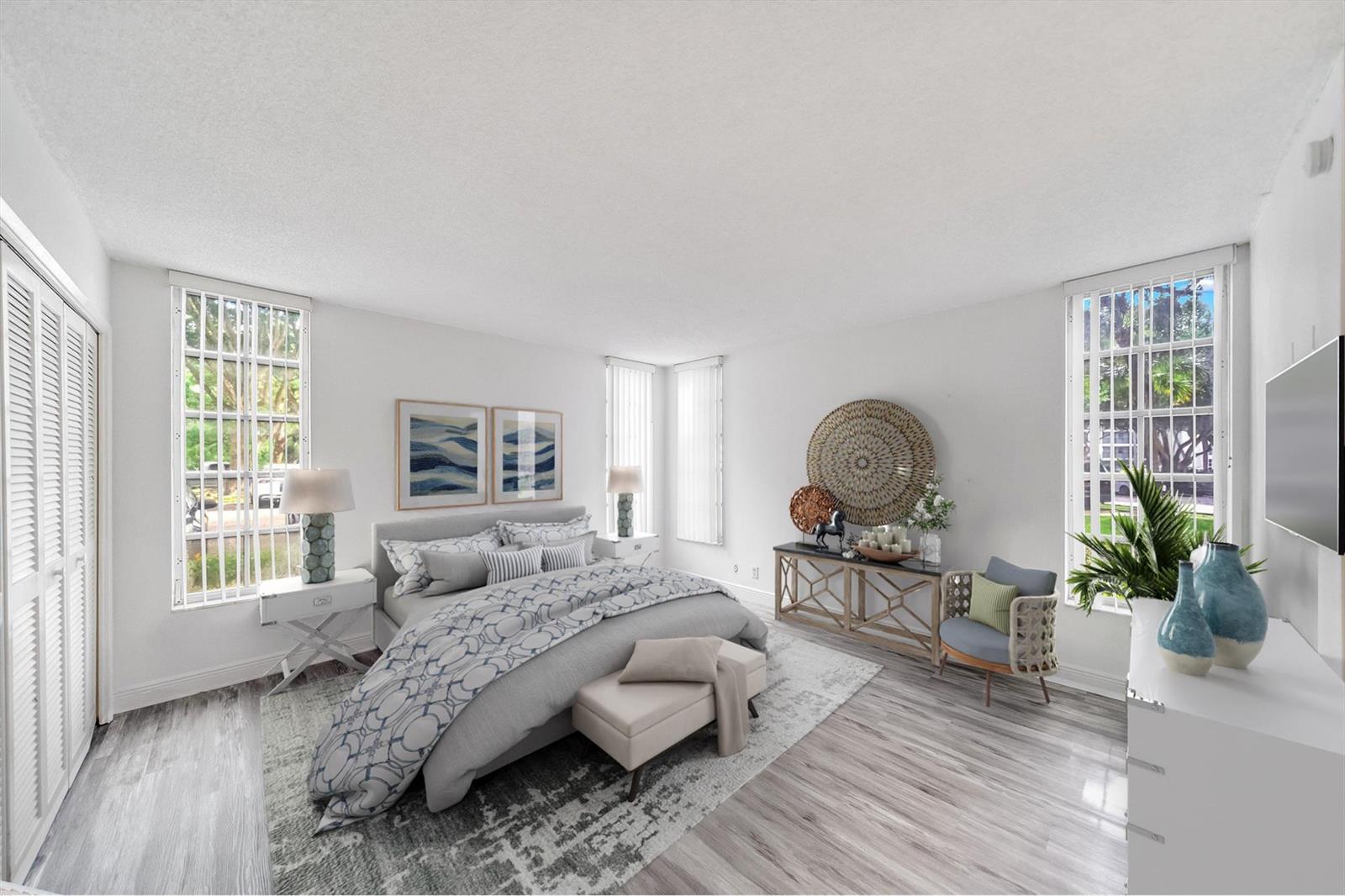 A bedroom features a bed, a console table, a chair, and windows with white blinds — 2601 S Course Drive # 111, Pompano Beach FL 33069, POMPANO BEACH, FL