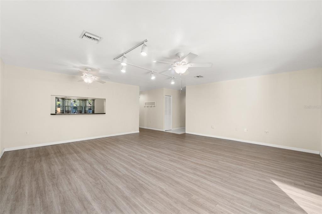 A spacious, empty room features light-colored walls, wood-look flooring, two ceiling fans, and track lighting — 1273 WOODBURY AVENUE, SEBRING, FL