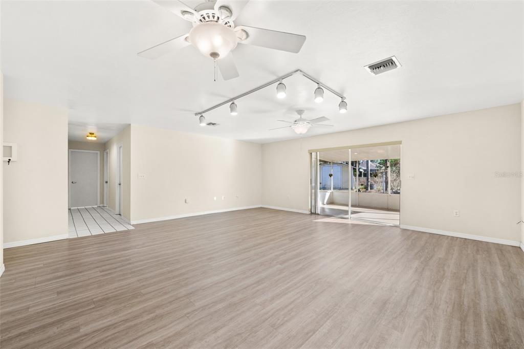 A spacious room with light wood-look flooring, a ceiling fan, track lighting, and sliding doors — 1273 WOODBURY AVENUE, SEBRING, FL