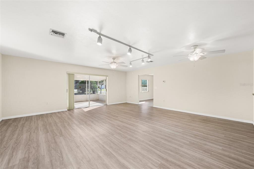 A spacious room with light wood-look flooring, track lighting, two ceiling fans, and sliding doors — 1273 WOODBURY AVENUE, SEBRING, FL