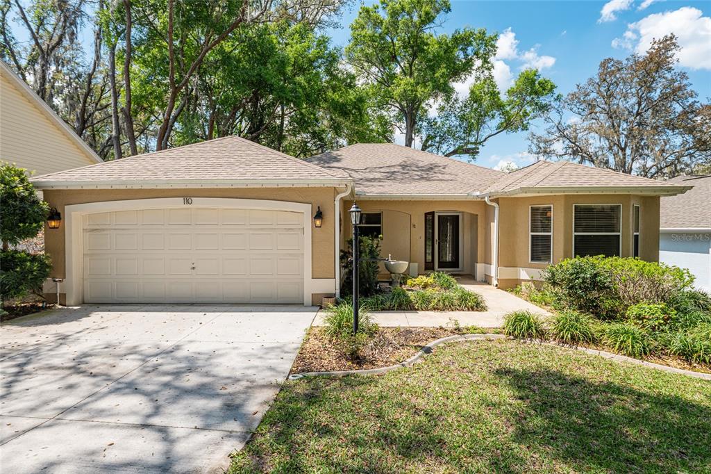 A single-story tan stucco house with a two-car garage and a front walkway — 110 CHULA VISTA AVENUE, LADY LAKE, FL