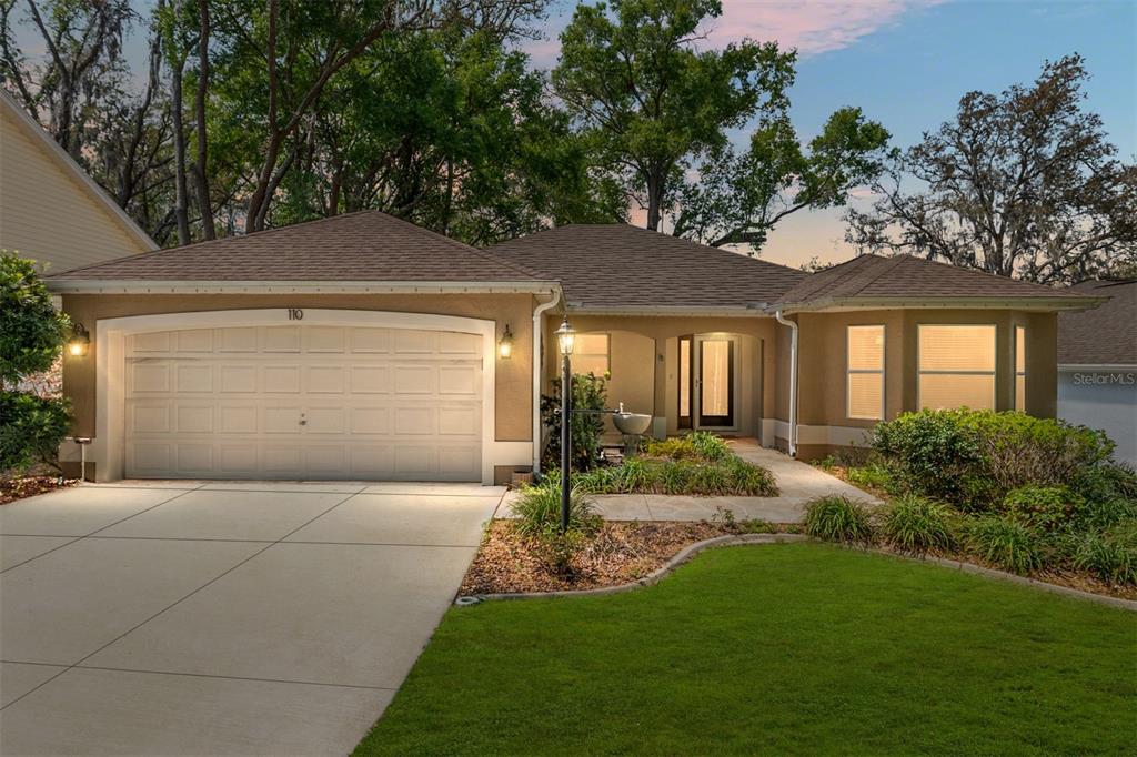A single-story house with a tan stucco exterior, a two-car garage, and a front lawn — 110 CHULA VISTA AVENUE, LADY LAKE, FL