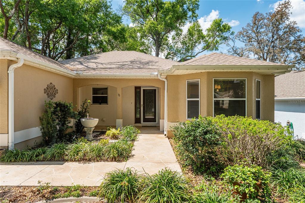 The exterior of a tan house features a covered entryway, a stone walkway, and landscaping — 110 CHULA VISTA AVENUE, LADY LAKE, FL