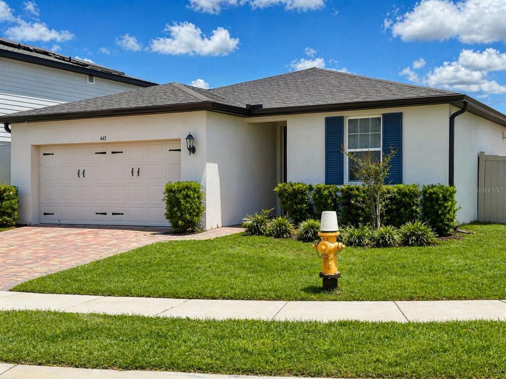 A single-story house with a white stucco exterior, blue shutters, and a yellow fire hydrant — 445 MCKENNA DRIVE, WINTER HAVEN, FL