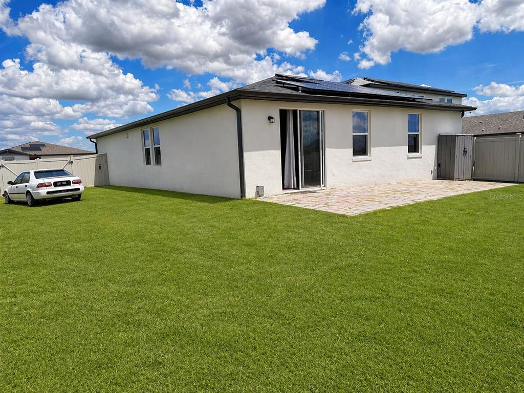 The exterior of a white stucco house features a patio, solar panels, and a backyard — 445 MCKENNA DRIVE, WINTER HAVEN, FL