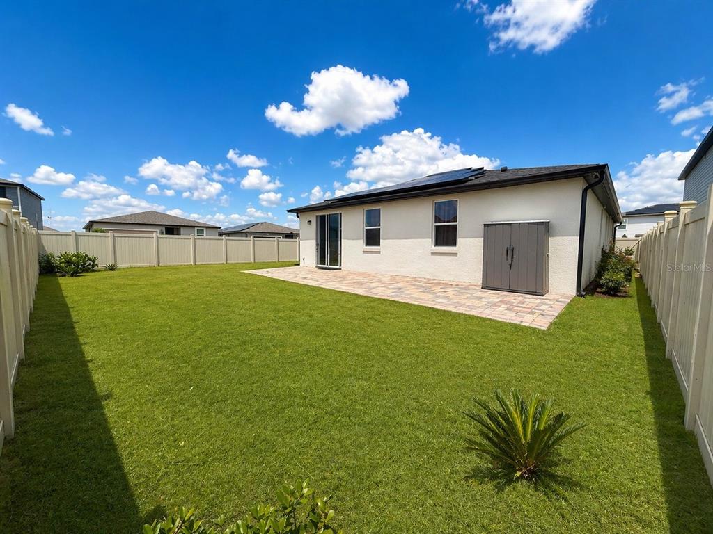 A backyard with a paved patio, a storage shed, and a white vinyl fence — 445 MCKENNA DRIVE, WINTER HAVEN, FL
