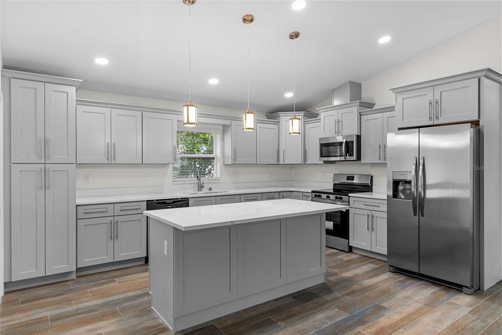 A modern kitchen features light gray cabinets, a white quartz island, and stainless steel appliances — 5160 80TH WAY N, ST PETERSBURG, FL
