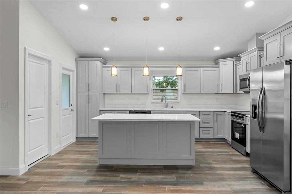 A modern kitchen features light gray cabinets, a white island, and stainless steel appliances — 5160 80TH WAY N, ST PETERSBURG, FL