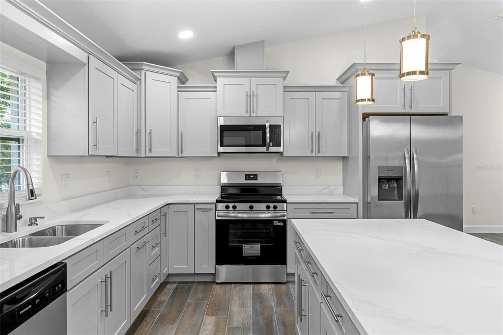 A kitchen features light gray cabinets, white marble-look countertops, stainless steel appliances, and wood-look flooring — 5160 80TH WAY N, ST PETERSBURG, FL